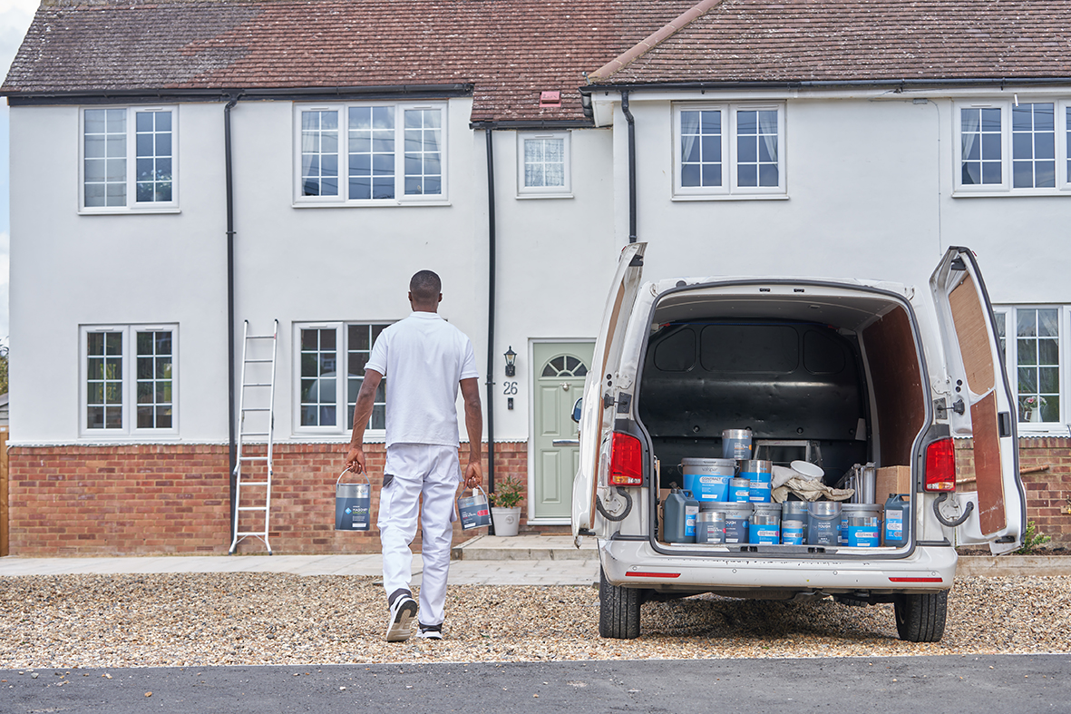 Open van with bottles and tub inside, and man carrying paint tins towards house